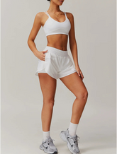 Mulher vestindo o Conjunto Maitê branco, composto por top de alças duplas e short com cintura elástica e bolsos laterais. Look moderno, ideal para treinos ou uso casual.






