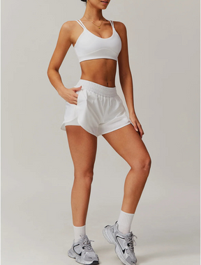 Mulher vestindo o Conjunto Maitê branco, composto por top de alças duplas e short com cintura elástica e bolsos laterais. Look moderno, ideal para treinos ou uso casual.






