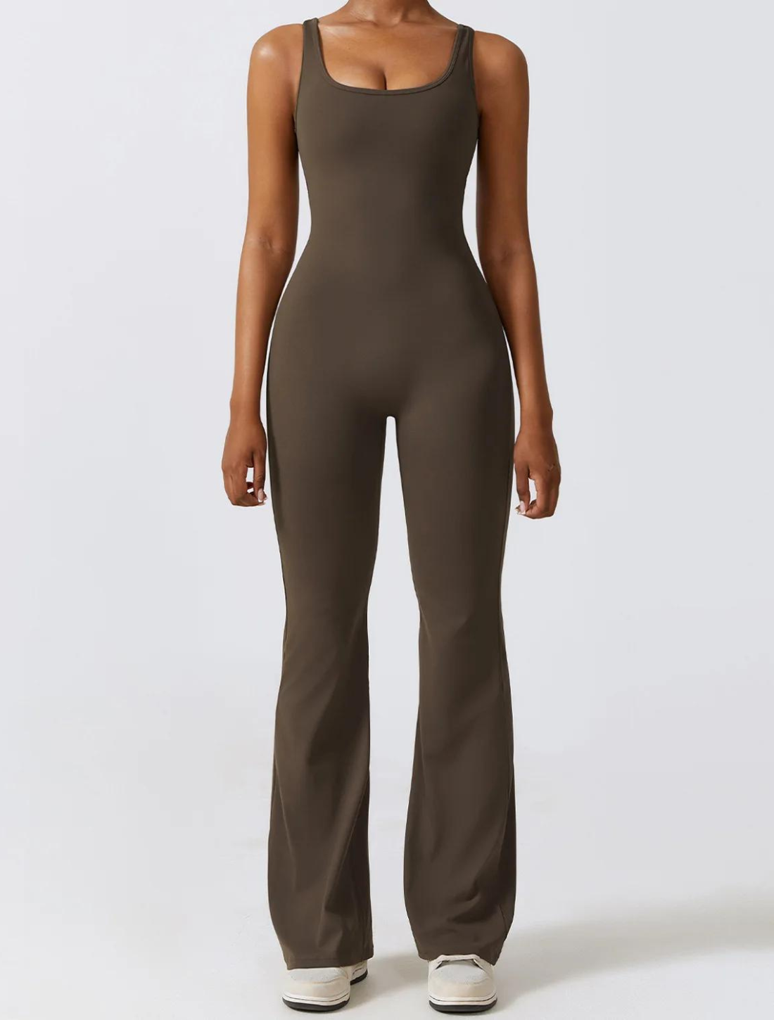 Mulher vestindo um macacão fitness marrom de tecido ajustado e confortável, com design de alças largas, pernas alongadas e corte elegante, ideal para atividades físicas ou casual.