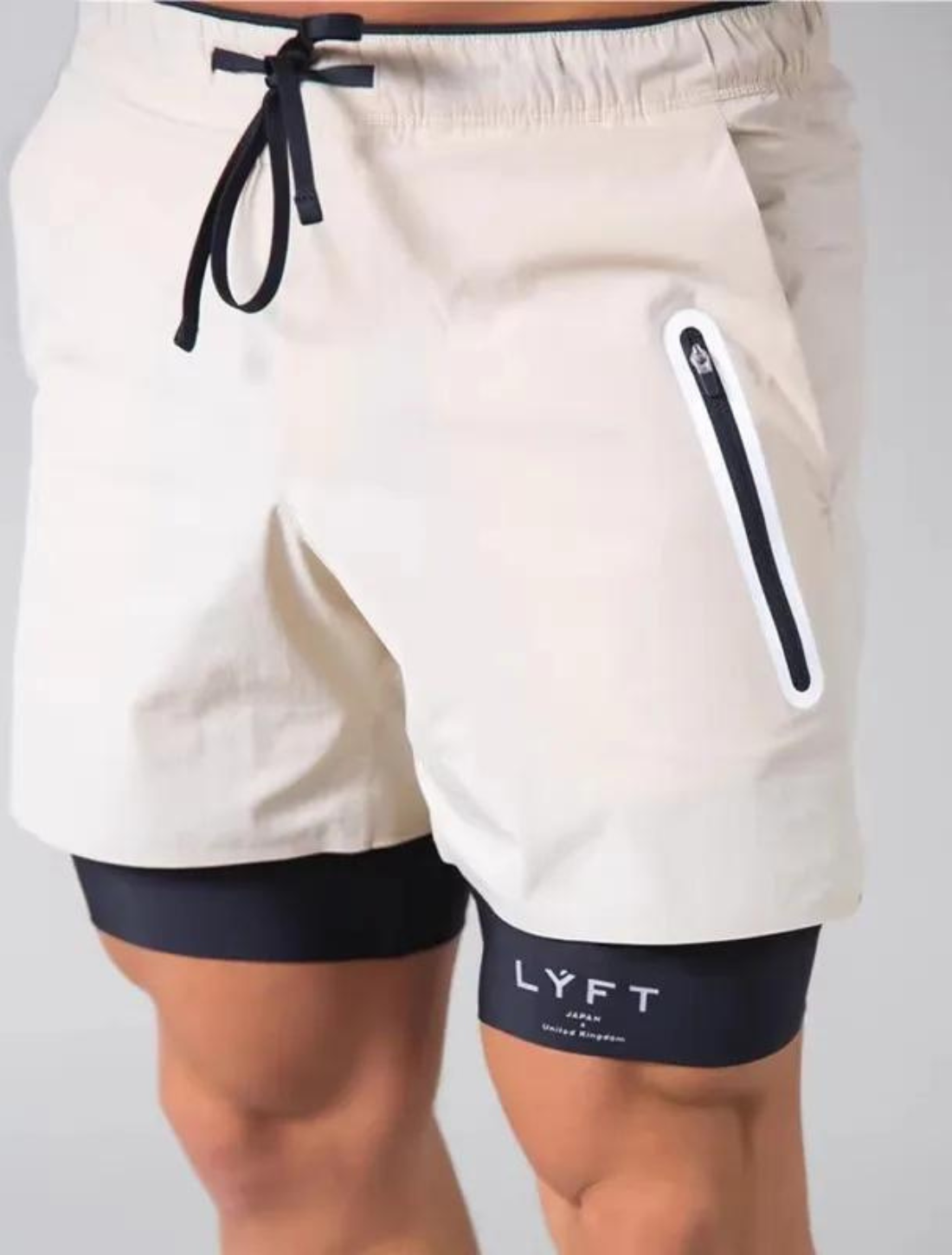 Short Urban Premium 2 em 1 na cor bege, com camada externa leve, bolso com zíper e cordão ajustável. Camada interna preta de compressão com logo "LYFT".